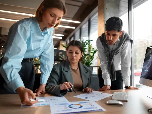 three people over a desk reviewing business intelligence materials.